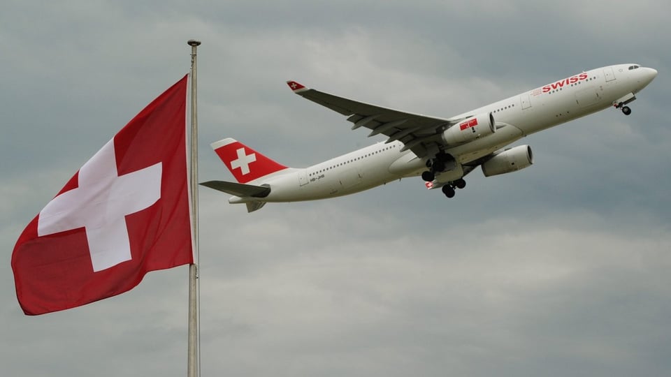 Eine Maschine der Swiss fliegt hinter einer Schweizer Flagge vorbei.