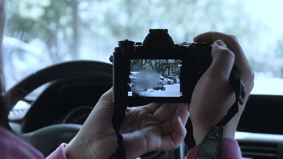 Eine NDB Mitarbeiterin sitzt im Auto und observiert einen möglichen Gefährder mit der Kamera in der Hand. 