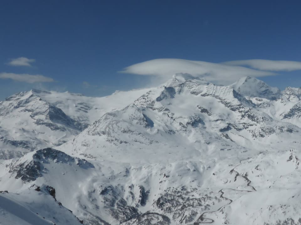 Verschneite Berge und über einem Gipfel eine linsemförmige Wolke. Der Himmel ist dabei stahlblau.