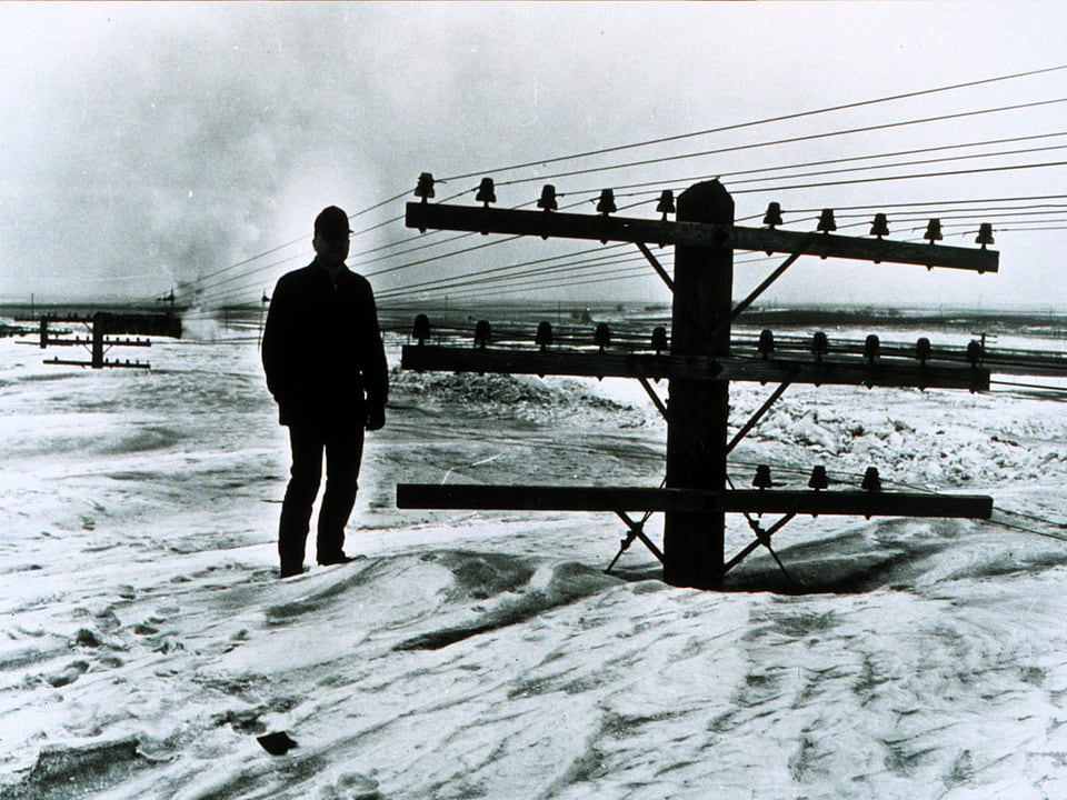 Auf einem alten Bild sieht man einen Mann auf meterhohem Schneee stehen. Neben ihm ragt nur noch die Spitze eines Strommasten heraus.