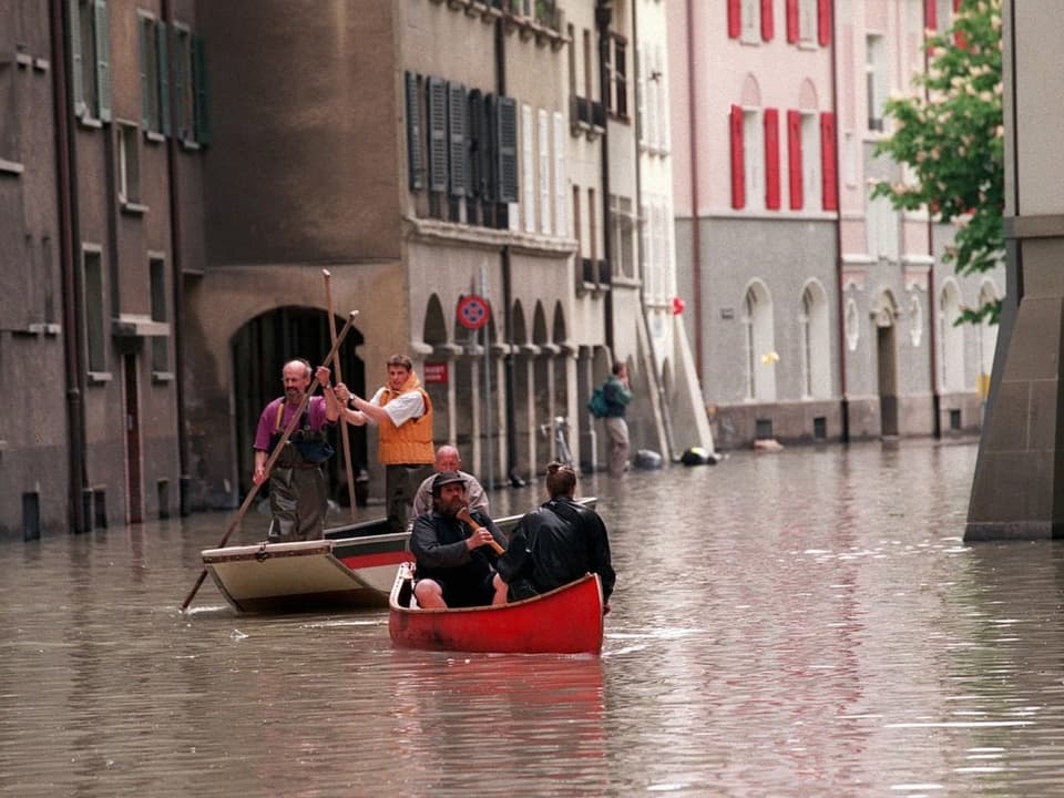Menschen in Booten auf einer überfluteten Stadtstrasse