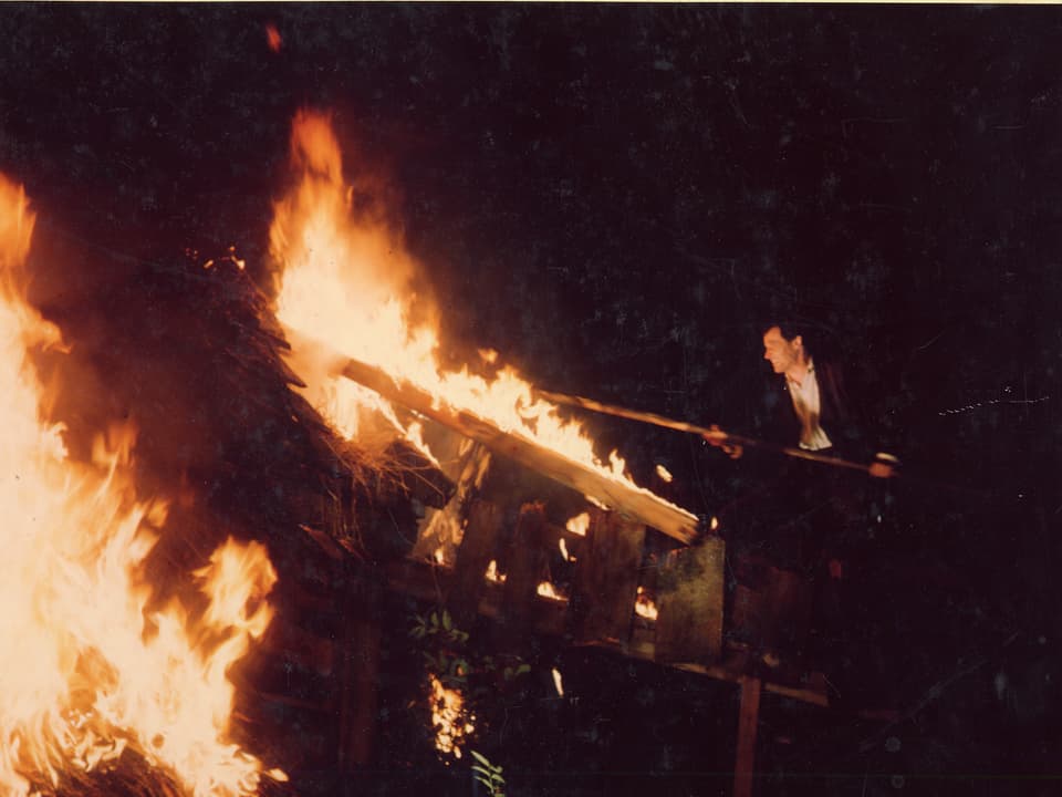 Christen stochert mit einer Bohnenstange im Feuer eines Hauses.