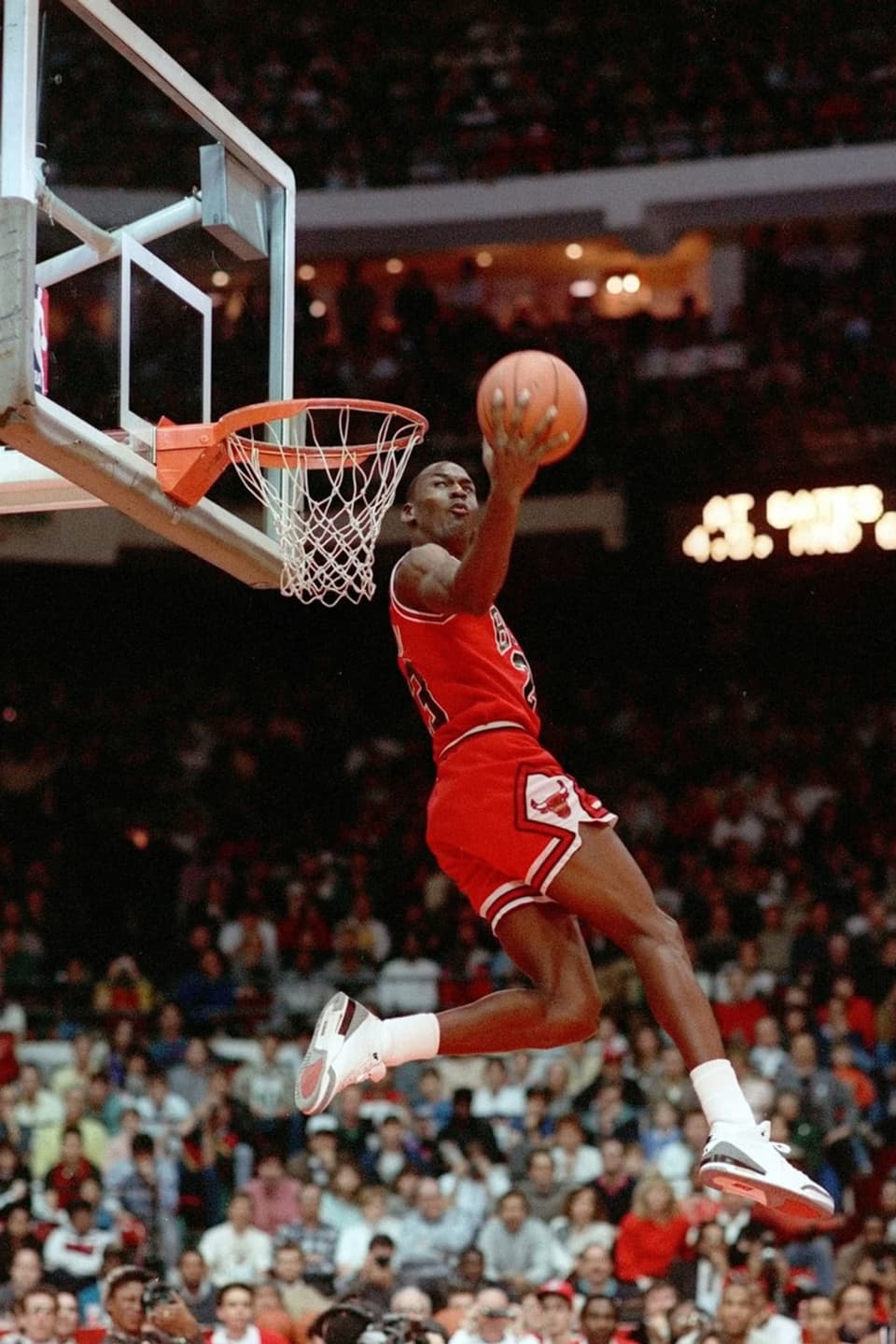 Ein Mann in roter Sportkleidung fliegt rückwärts auf einen Basketballkorb und versenkt den Ball sicher im Korb.