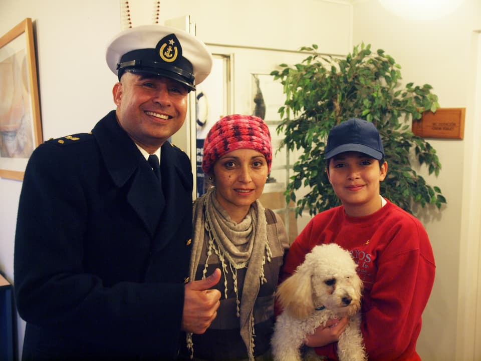 Ein Mann in Marineoffiziers-Uniform, eine Frau und ein Junge, der einen Hund im Arm hält. 