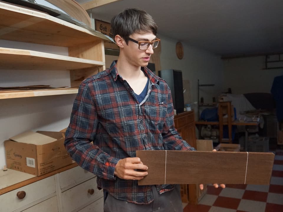 Ein junger Schreiner mit einem Stück Holz in seinem Atelier.