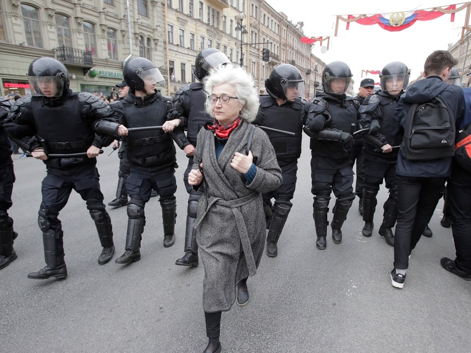 Eine ältere Dame läuft von einer Truppe Polizisten arm-in-arm. 