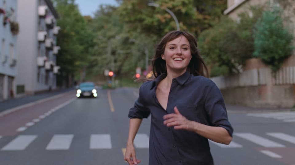Julie (Renate Reinsve) rennt auf offener Strasse lachend der Kamera entgegen.