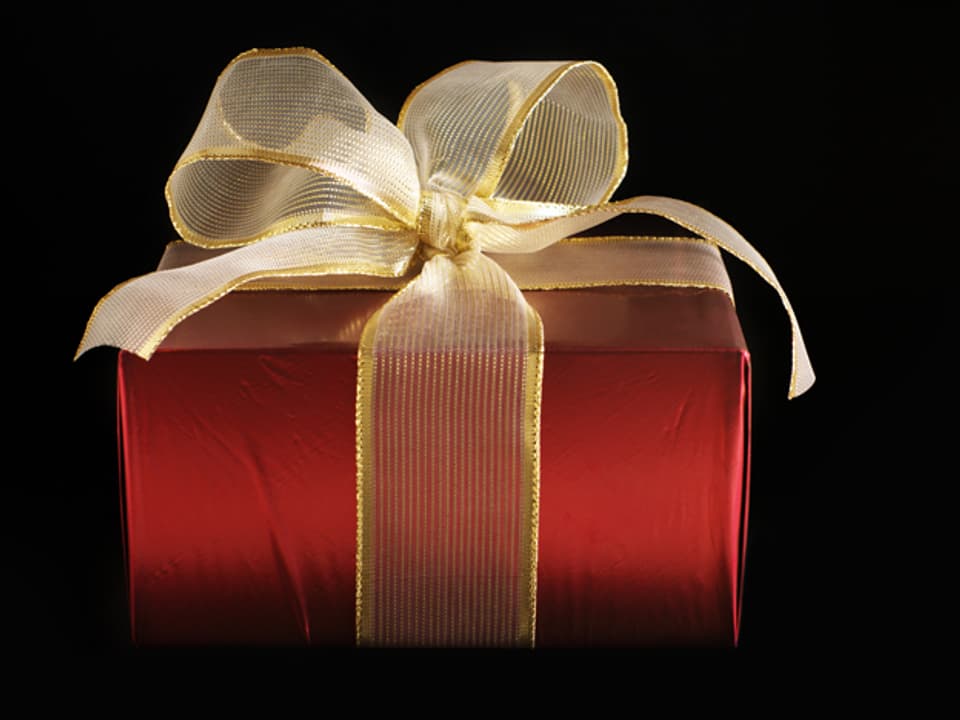 Ein rotes Geschenk mit goldener Schlaufe vor schwarzem Hintergrund.