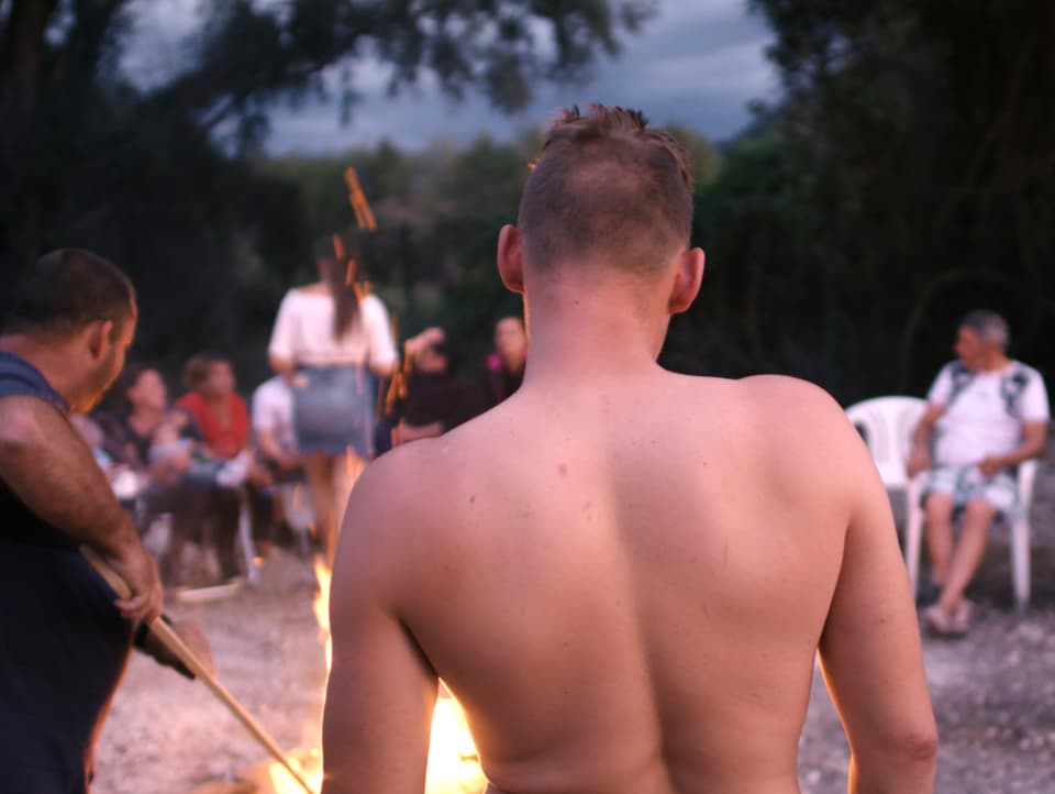 Der nackte Rücken eines jungen Mannes vor einem Fest um ein Feuer