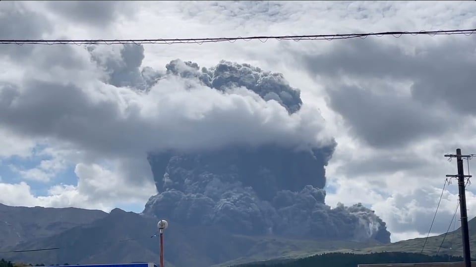 Eine graue Aschevolke türmt sich über einem Vulkan auf.