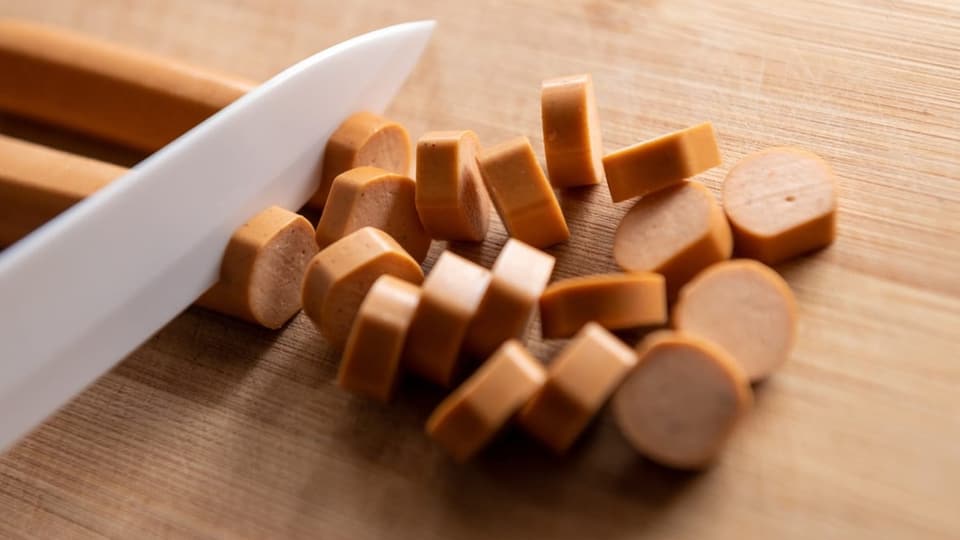 Jemand schneidet eine Vegiwurst in Scheiben.