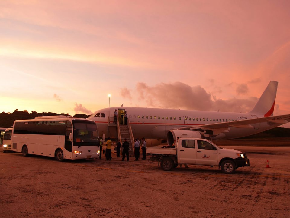 Flugzeug mit Bussen und anderen Fahrzeugen vor abendrotem Himmel.