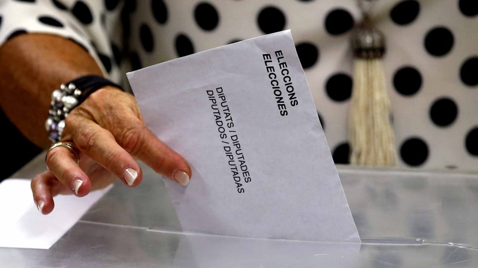 Eine Frauenhand wirft den Wahlzettel in die Urne.