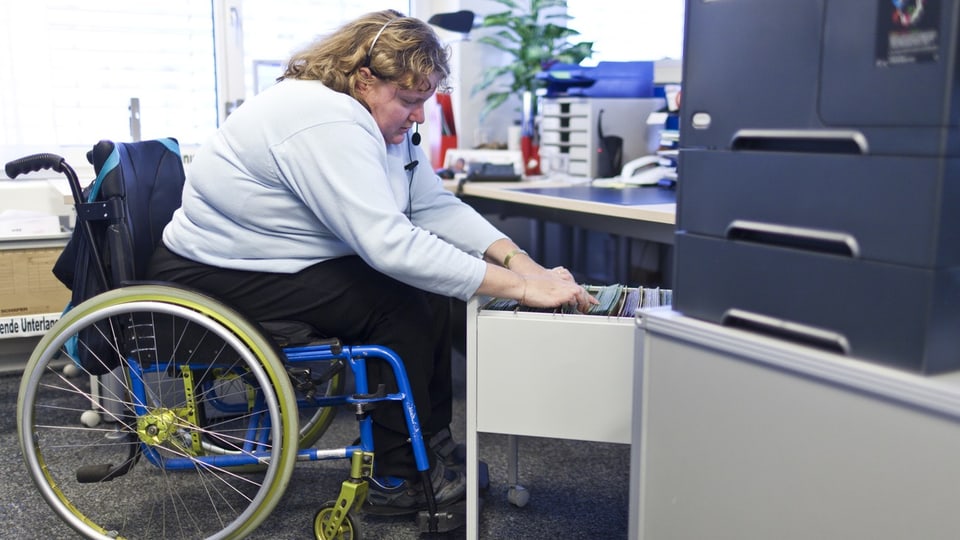 Eine Frau im Rollstuhl arbeitet in einem Büro.