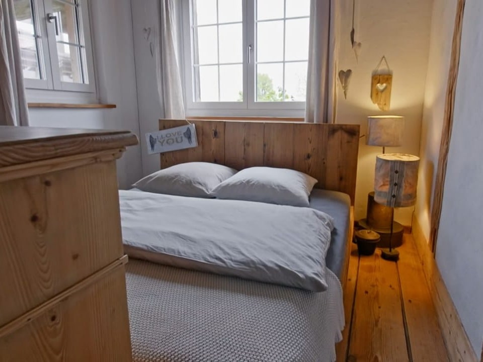 Ein Schlafzimmer, weisses Bett und älterer Parkettboden und ein Bauernschrank.