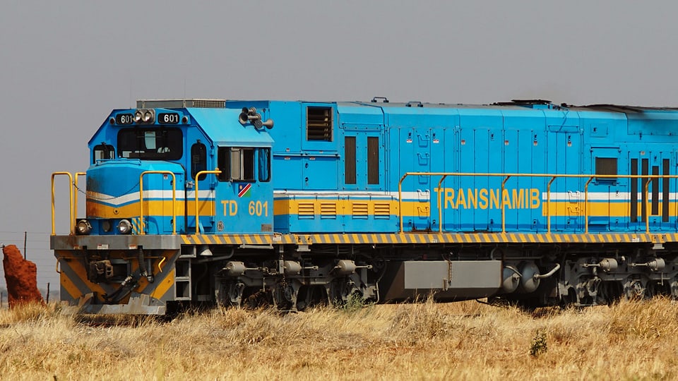 Ein türkisfarbener Zug fährt durch eine trockene Landschaft.