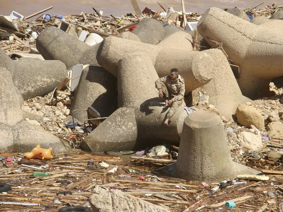 Ein Mann sitzt inmitten riesiger Steintrümmer und angeschwemmten Abfall-und Holzresten.