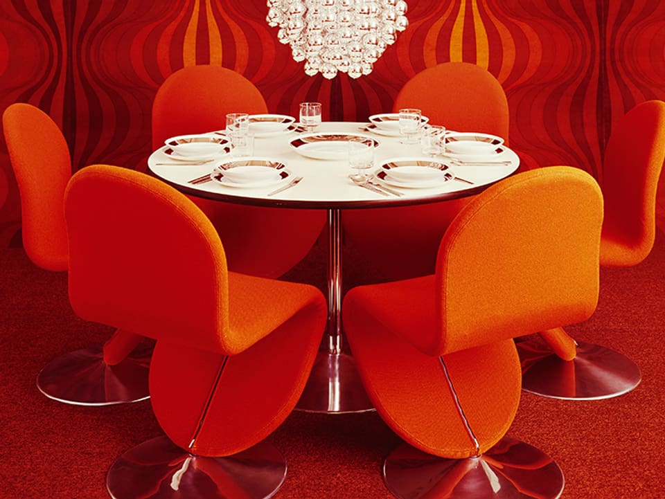 Weisser Tisch mit orangen Stühlen in Zimmer mit orangen Tapeten und orangem Teppich