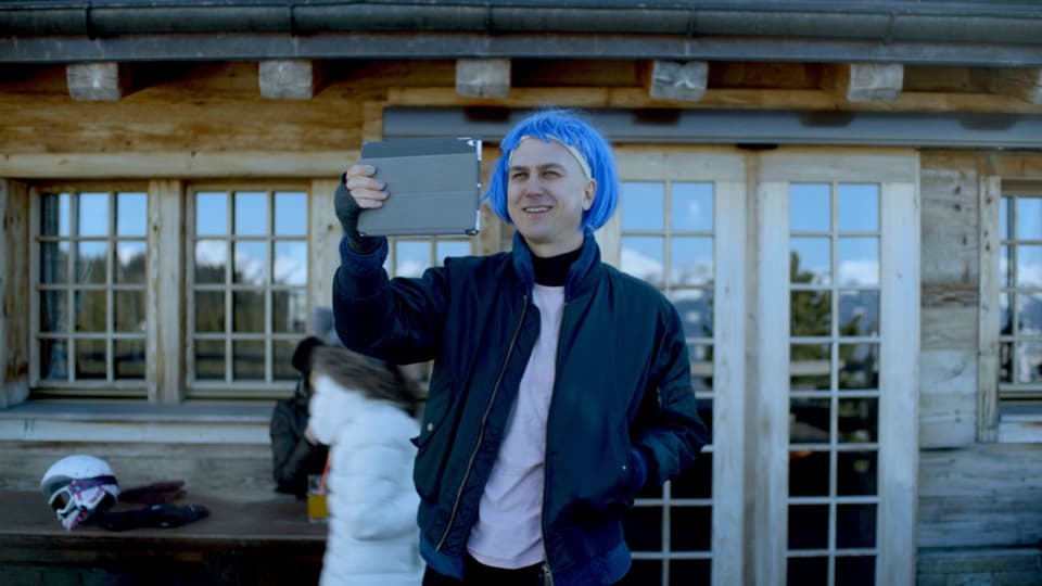 Mann mit blauer Perücke und Handy vor einem Haus