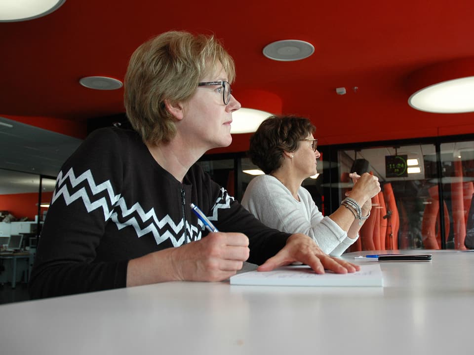 Zwei Frauen sitzen mit Notizpapier am Sitzungstisch.