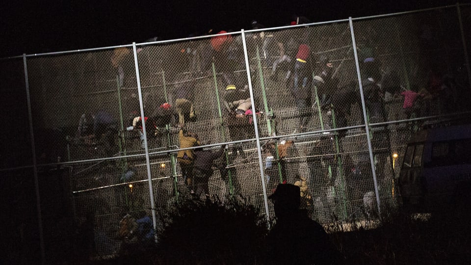 Migranten klettern über den Grenzzaun. 
