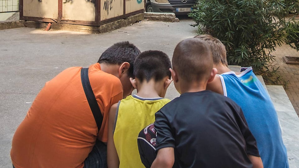 Vier Jungen schauen gemeinsam auf ein nicht sichtbares Smartphone