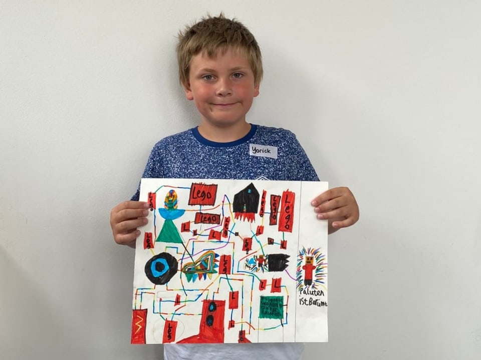 Ein Junge hält eine Zeichnung vor sich. Darauf ist eine Stadt im Lego-Regen zu sehen.