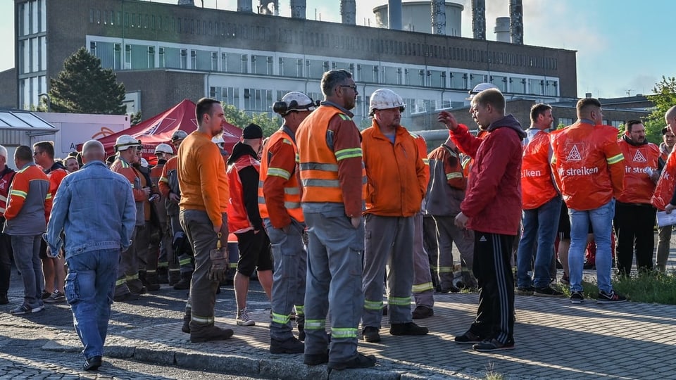 Versammelte Arbeiterinnen und Arbeiter vor einer Stahlfirma.