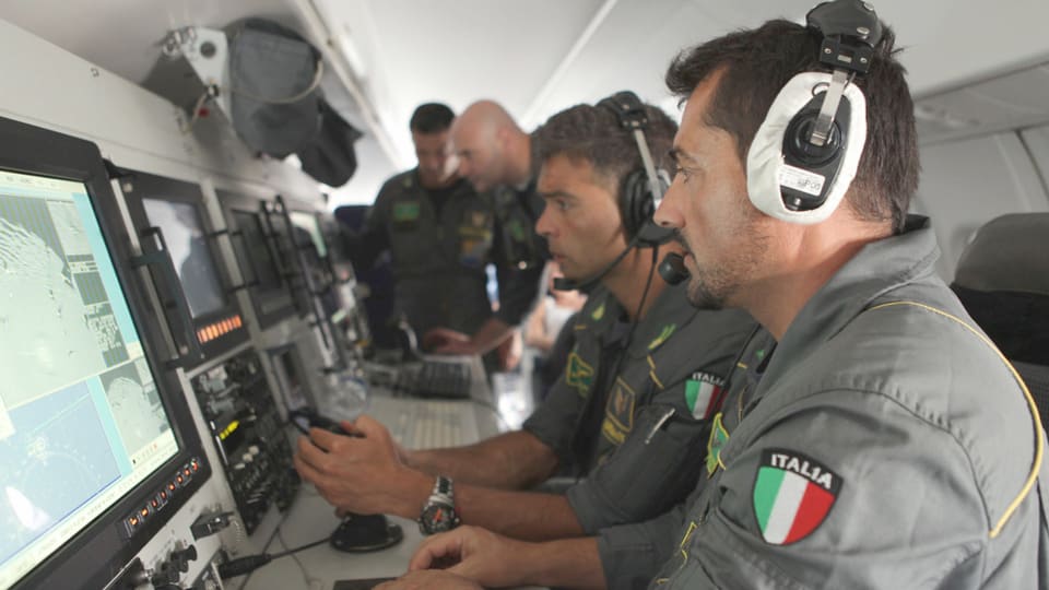 Italienische Polizisten kontrollieren in einem Flugzeug Monitore.