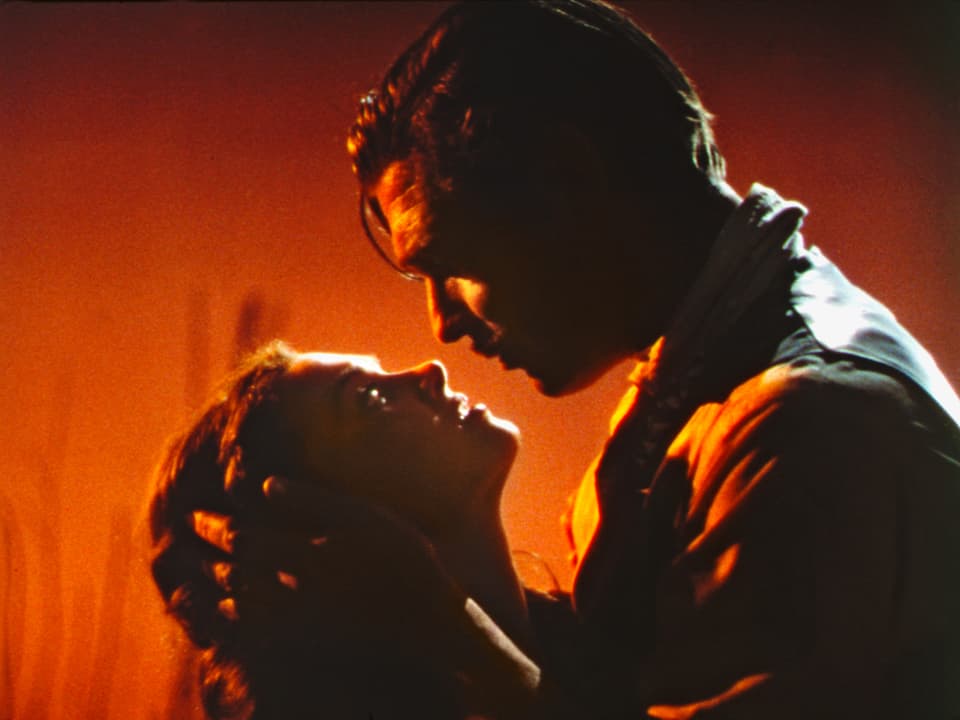 Vivien Leigh und Clark Gable in inniger Umarmung vor rotem Hintergrund.