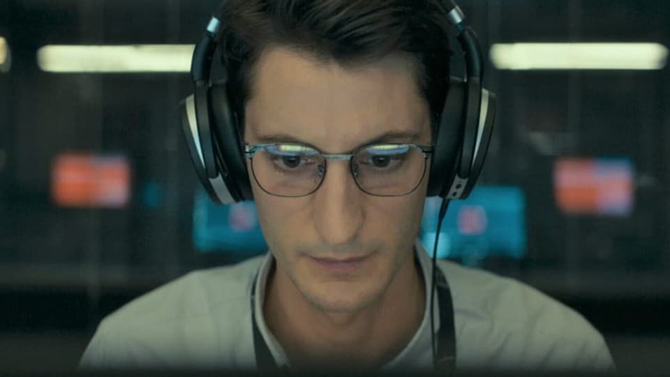 ein Mann mit Brille und Kopfhörern ist in einem Raum mit mehreren Computern.