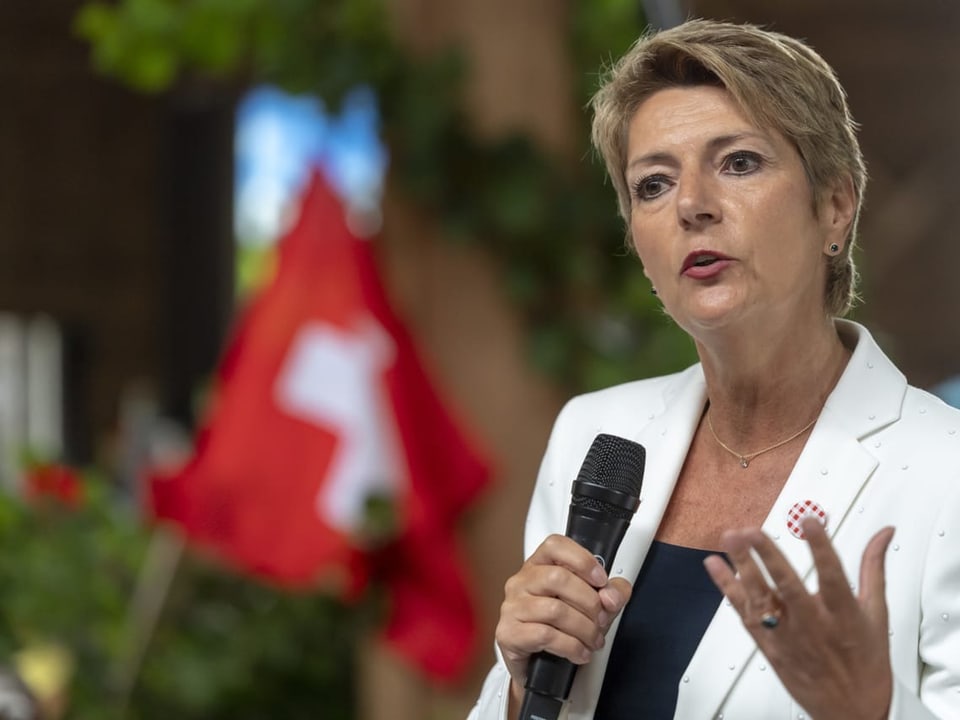 Karin Keller-Sutter hält ihre Ansprache mit Mikrofon in der Hand. Im Hintergrund: Schweizer Flagge.