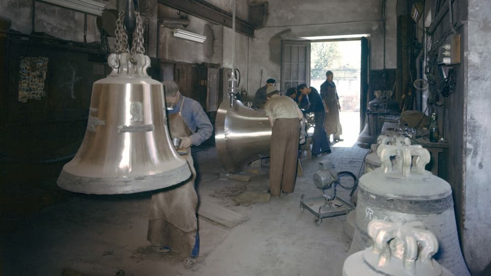 Grosse Glocken hängen vor Arbeitern an der Decke.