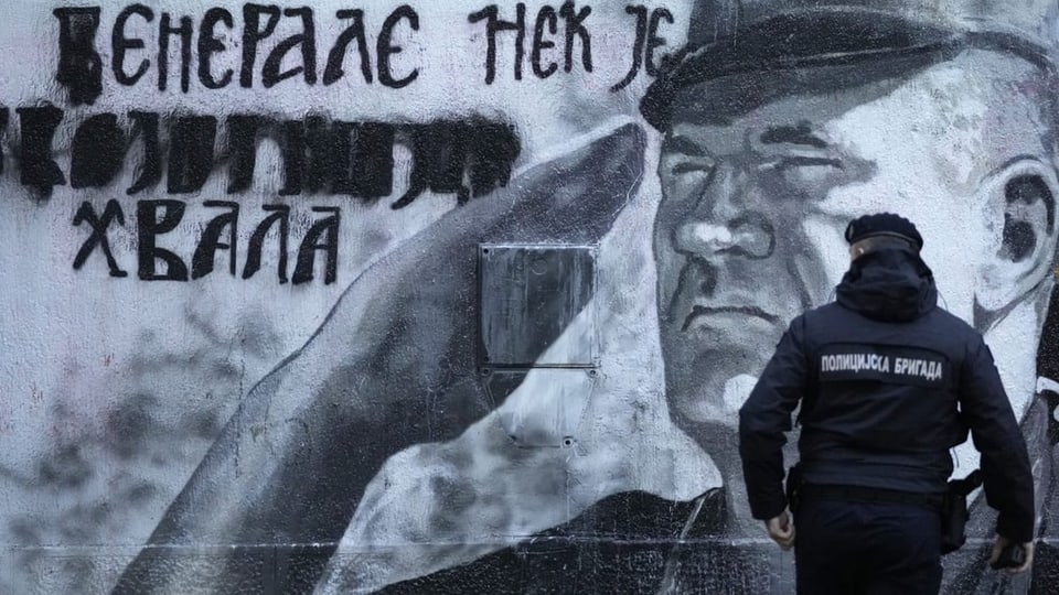 Mladić-Wandbild, ein Polizist steht davor.