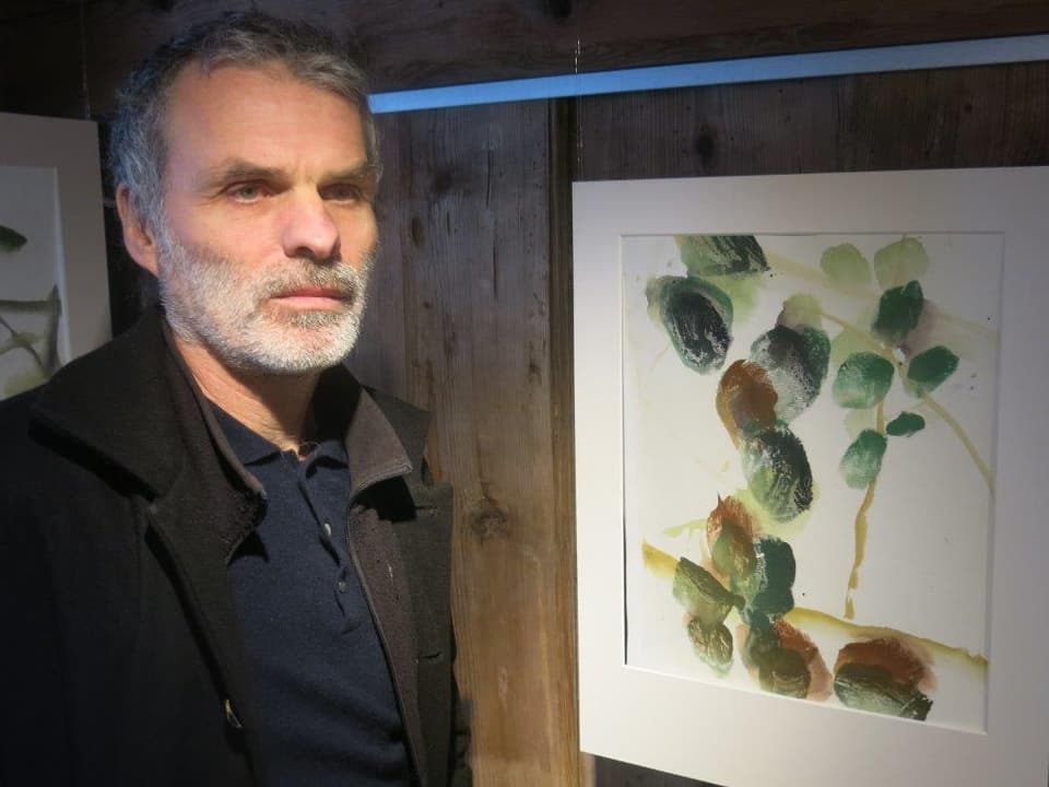 Der Maler Ivo Vonlanthen steht vor einem Bild, das wie ein Zweig mit Blättern aussieht.