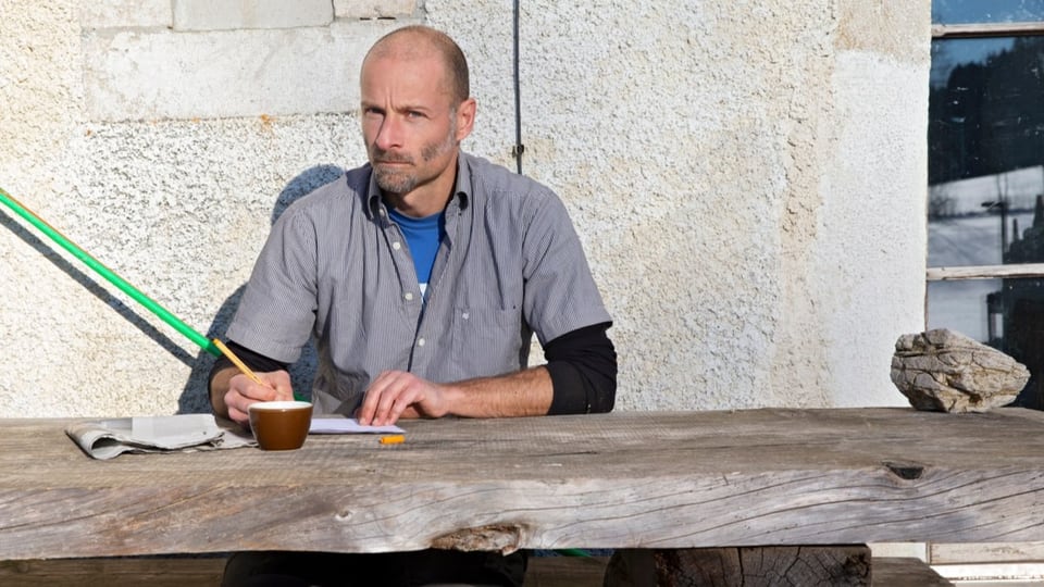 Mann schreibt draussen an einem Holztisch