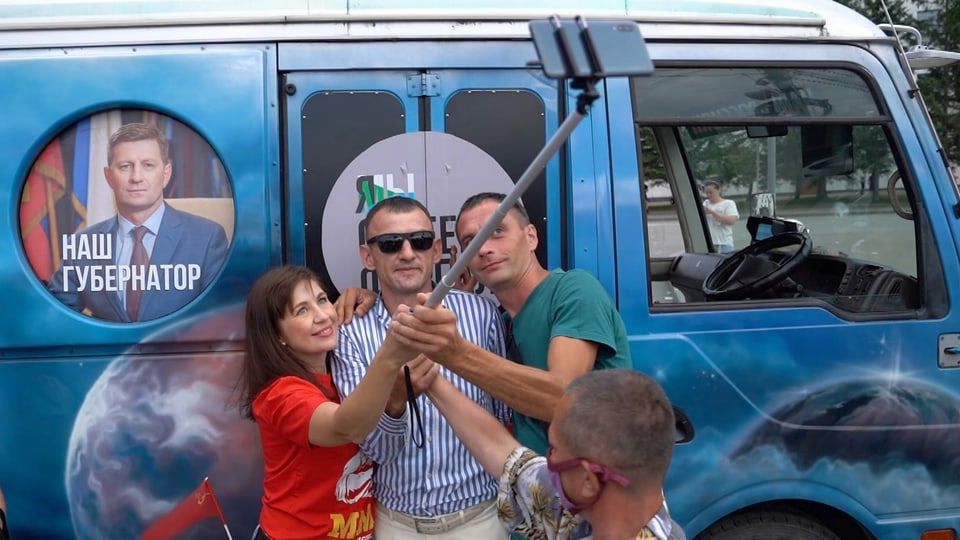 Drei Personen fotografieren sich vor einem blauem Kleinbus.