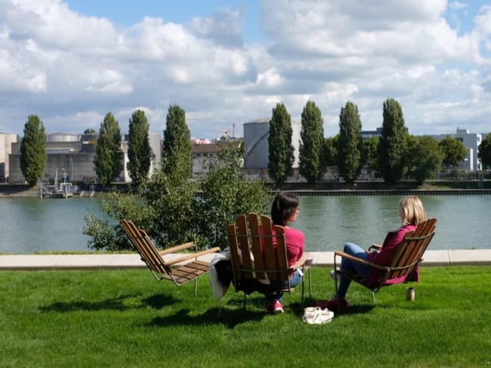 Leute liegen in Liegestühlen am Rheinbord auf dem Novartis-Campus.  