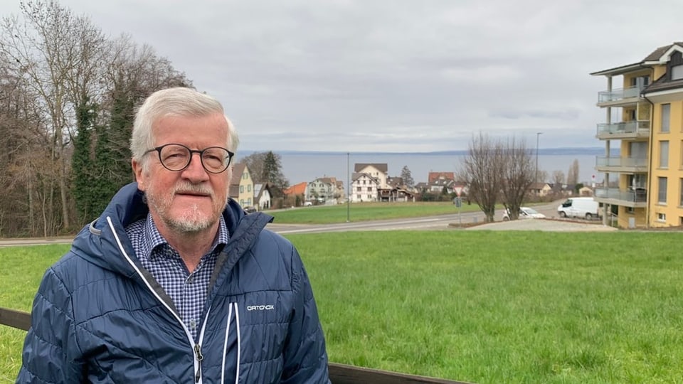 Ein älterer Mann steht draussen, hinter ihm sieht man den Bodensee in der Ferne.