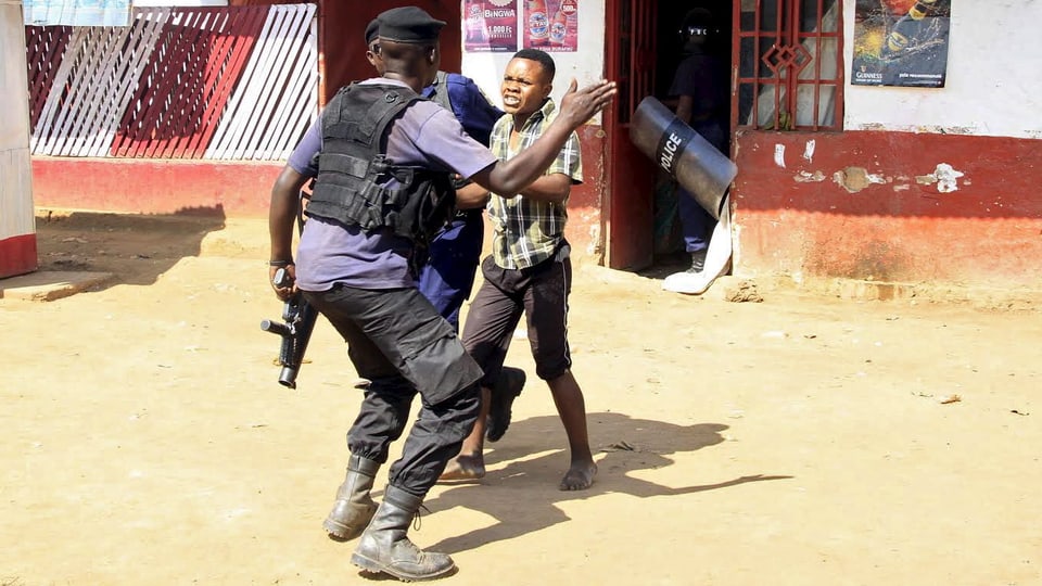 Ein Polizist mit erhobener Hand von hinten und ein Jugendlicher, der von einem anderen Polizisten festgehalten wird.