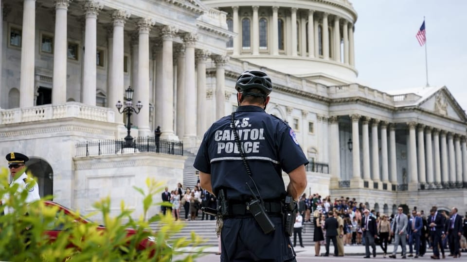 Ein Sicherheitsbeamter des US-Kapitols steht vor dem Gebäude, dahinter sind viele Menschen.