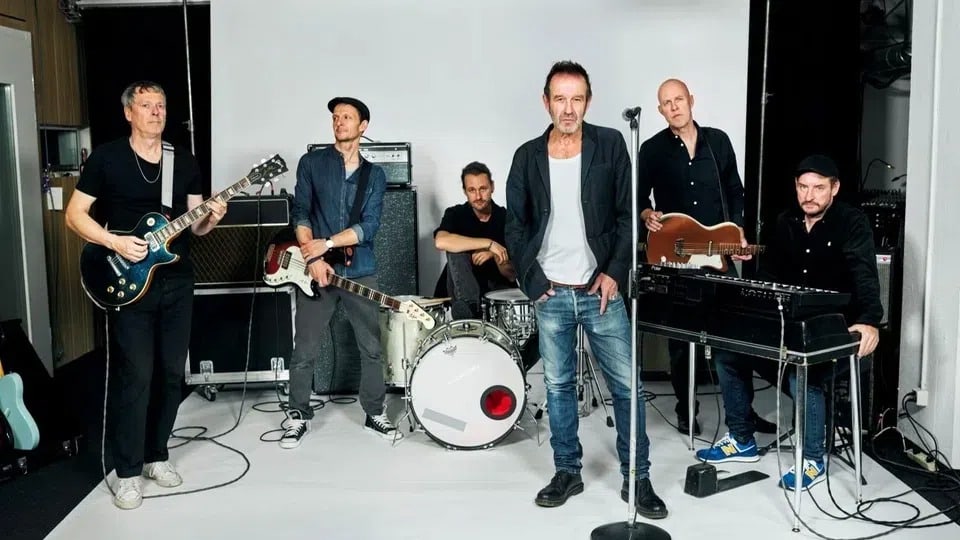 Eine Musikband mit sechs Musikern in einem Proberaum.