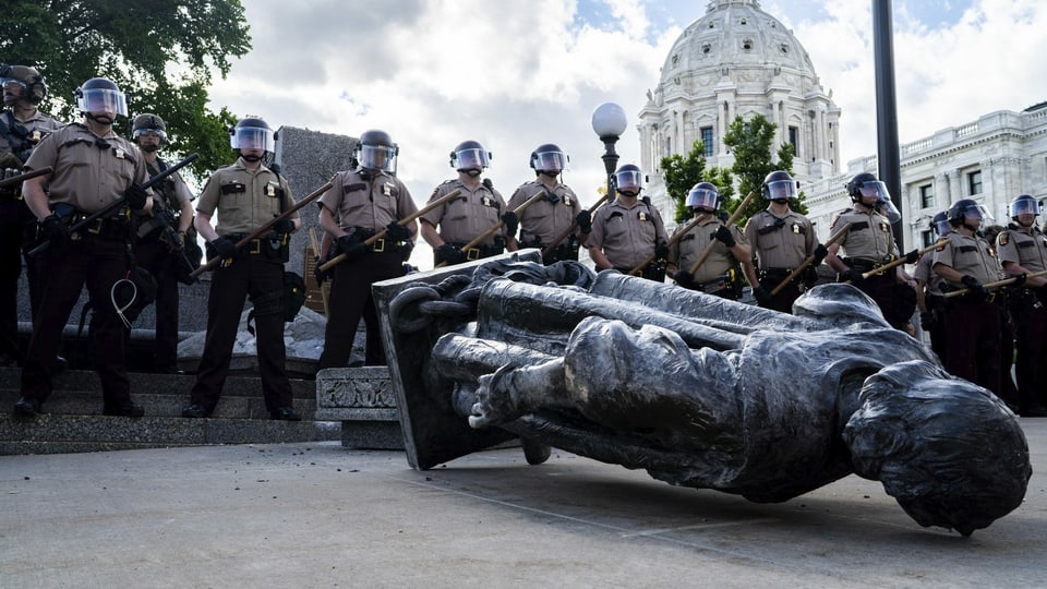 Polizisten stehen hinter der umgestossenen Statue