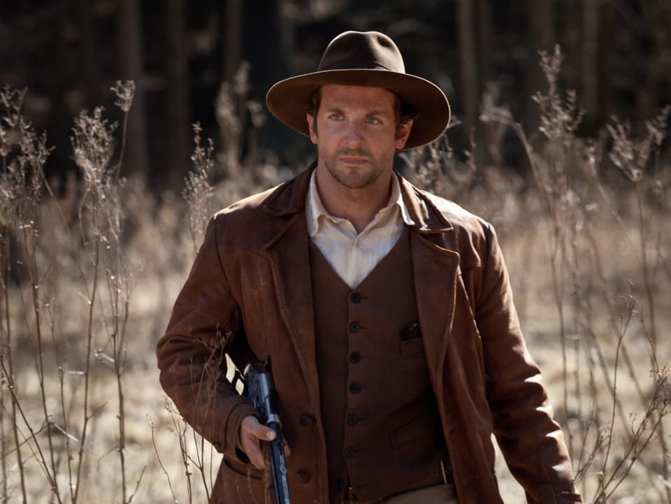 Bradley Cooper mit Hut und einem Gewehr.
