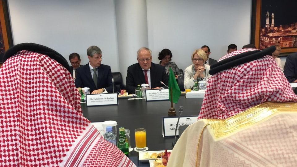 Schneider Ammann und Verterter der Schweizer Delegation beim Treffen zwischen zwei von hinten fotografierten Saudis im Bildvordergrund.