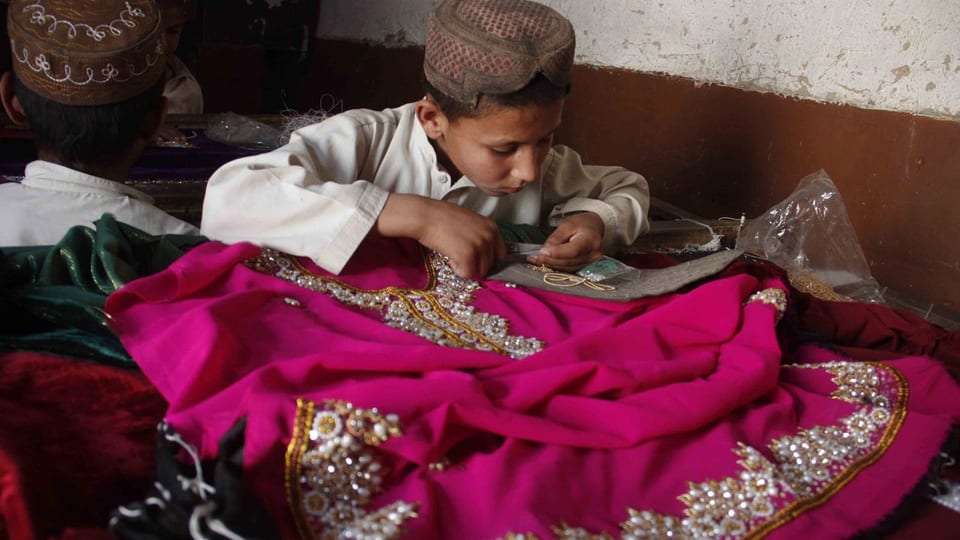 Ein kleiner Junger bestickt ein Kleidungsstück mit Perlen.