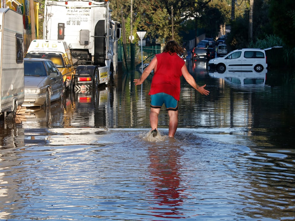 Eine Person watet durch eine überschwemmte Strasse.