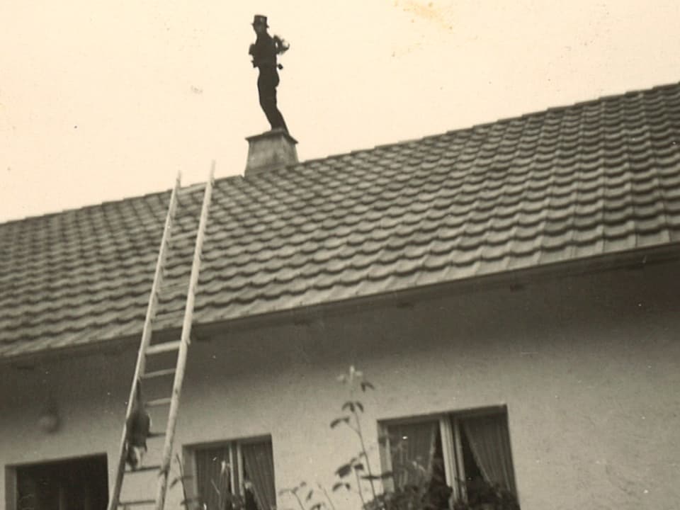 Ein Kaminfeger steht auf dem Dach auf einem Kamin.