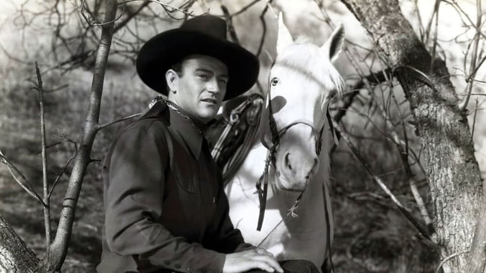 John Wayne als Tom Mix neben einem weisen Pferd.