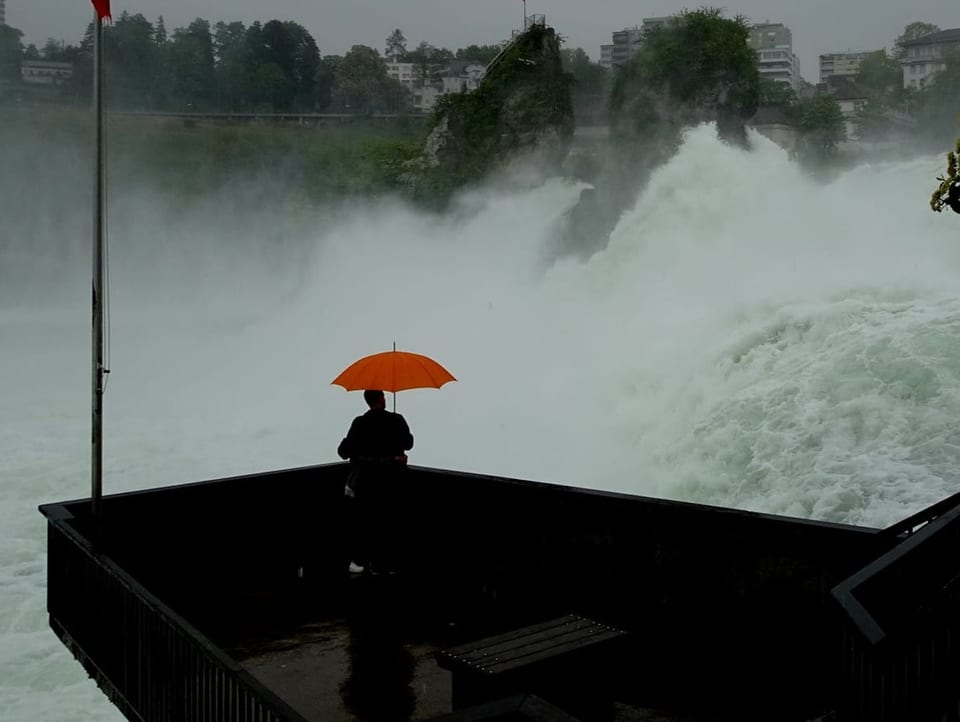 Grosser Wasserfall mit Aussichtsplattform mit Mensch mit Rengeschirm